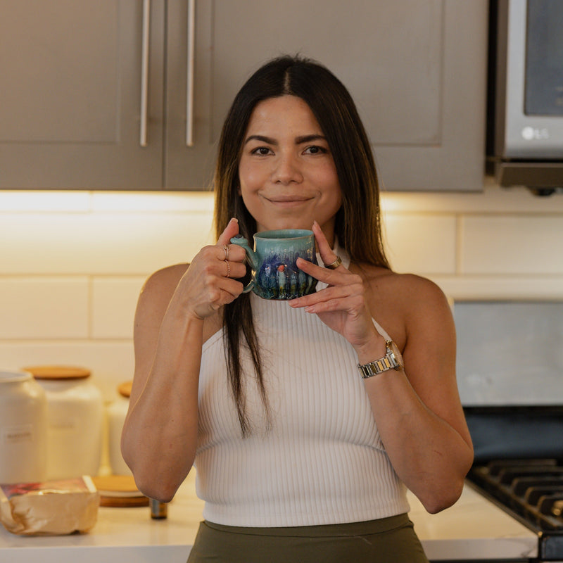 Woman taking a mirror selfie in a kitchen holding a mug.